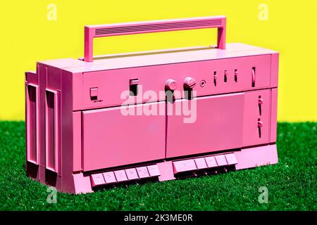 Bright pink vintage cassette player placed on green grass against yellow background in studio Stock Photo