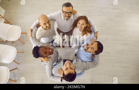 Group of happy smiling diverse colleagues hugging standing in circle and looking up. Stock Photo