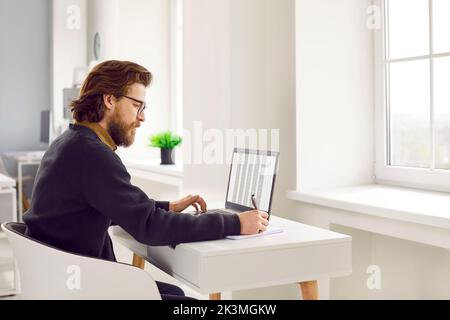Serious man in office working with databases using laptop and Excel spreadsheet. Stock Photo
