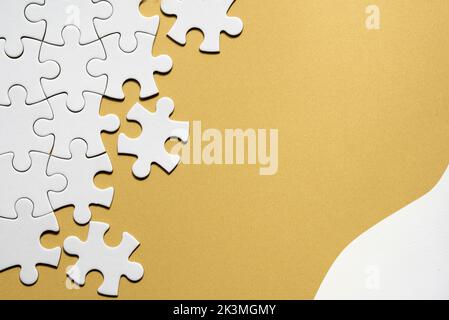 Jigsaw puzzle pieces half assembled and separate. Top view, flat lay on monochromatic abstract yellow white paper background. Copy-space, place for Stock Photo