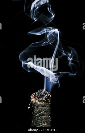 A vertical shot of the smoke of burning buffalo sage stick on black ...