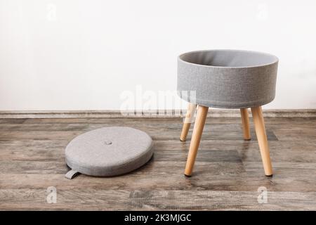 Trendy stool with and build-in storage space. Side view, white wall, copy space. Modern mulrifunctiional chair with wooden legs and removable lid. Round gray linen pouf Stock Photo