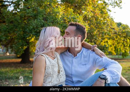 Couple in their 30s sitting in the park doing nose to nose, passionate moment Stock Photo