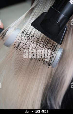 Young woman in a hairdressing salon dyes her hair blond and dries hair Stock Photo