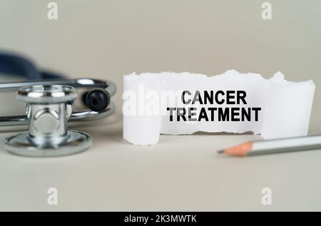 Medical concept. On a gray background, a stethoscope, a pencil and a paper plate with the inscription - CANCER TREATMENT Stock Photo