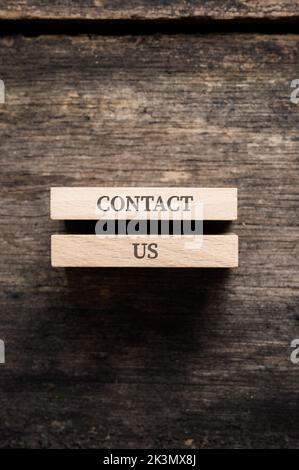 Contact us sign written on two wooden pegs placed over rustic wooden background. Stock Photo