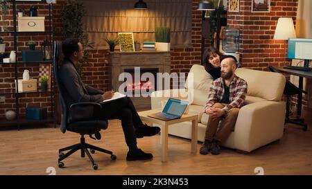 Psychotherapist consulting married couple at therapy session, taking notes to give professional guidance and counseling. Displeased man and woman talking about problems and divorce. Stock Photo