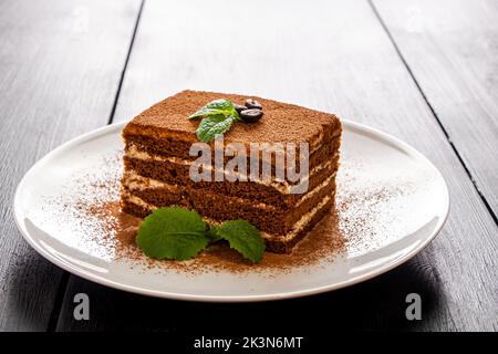 Tiramisu dessert decorated with mint on white plate. Slice of coffee cake on light background. Traditional Italian creamy dessert. Stock Photo