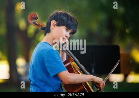 A beautiful boy plays cello in park Stock Photo