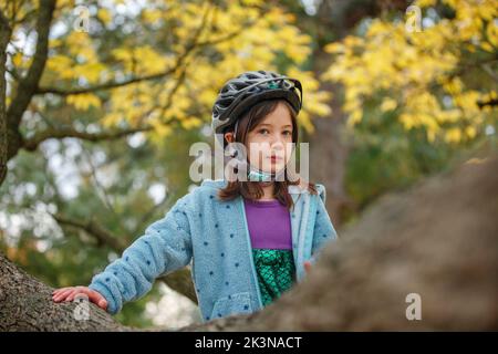 A small girl in bike helmet sits proudly in tree branches Stock Photo