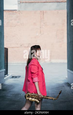 young girl in a pink jacket with a saxophone in her hand Stock Photo