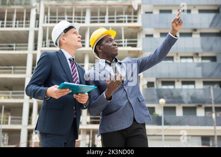 Two architects inspect the construction of new building. One of them points his hand to side Stock Photo