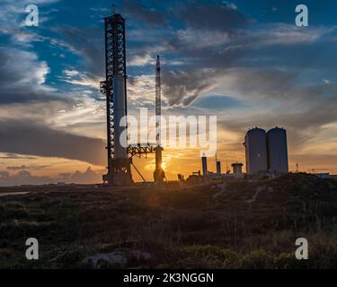 SpaceX launch pad including mechazilla tower and starship silhouetted by beautiful sunset and blue sky from sand dunes on Boca Chica Beach Stock Photo