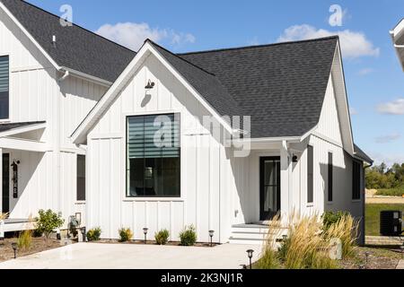 A small, ranch style modern farmhouse with white vertical siding, black ...