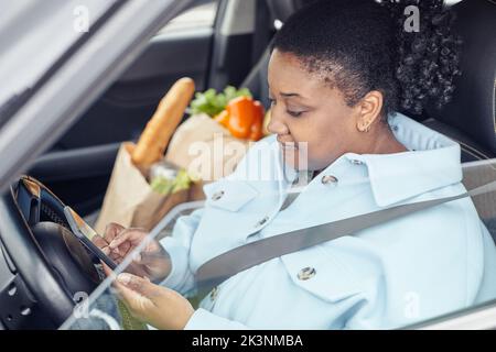 Side view portrait of young black woman using smartphone in car with safety belt Stock Photo