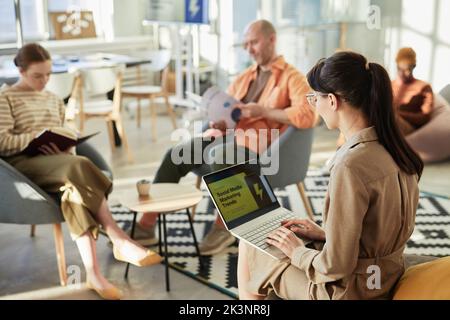 Side view portrait of young woman typing at laptop with marketing statistics on screen in company office, copy space Stock Photo