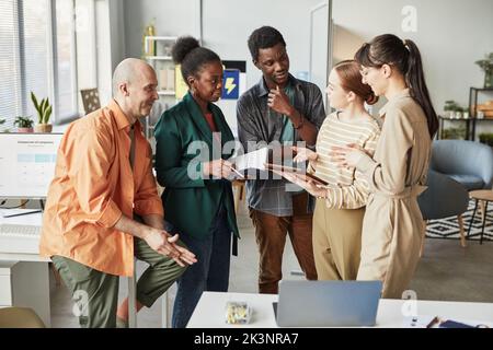 Portrait of diverse business team in office standing in circle and discussing project Stock Photo