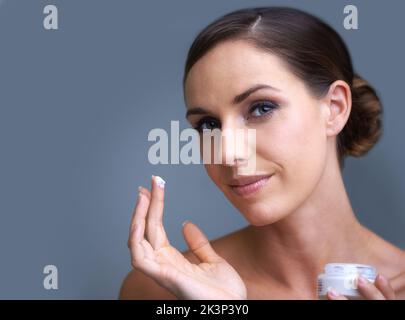 Maintaining her youth through anti-aging skin care products. Portrait of an attractive young woman applying moisturizer to her skin. Stock Photo