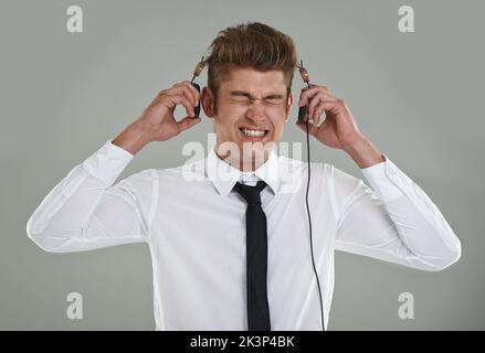 Turn it down. A young man pulling his headphones away from his ears while squinting his eyes shut. Stock Photo