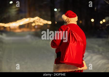 Back view of traditional Santa Claus carrying bag with presents at night in city, copy space Stock Photo