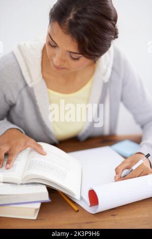 Taking down some important notes. Closeup shot of a pretty college student taking notes from her textbook. Stock Photo