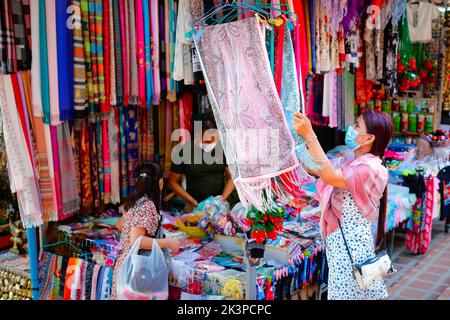 Chiangmai, Thailand - January 1, 2022: Lady with mask are choosing handmade colorful scarf in local shop on street where selling traditional product o Stock Photo