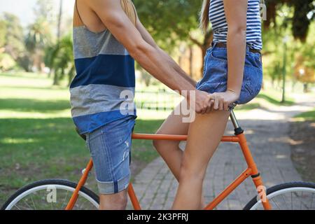Hipsters in love. Cropped image of a young couple riding a bike in the park. Stock Photo