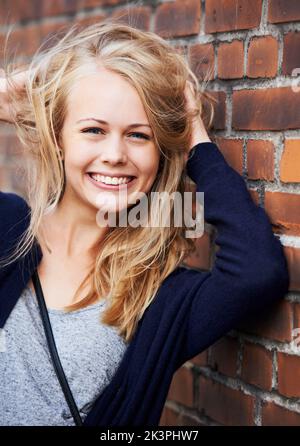 Confident and beautiful. Portrait of an attractive young woman leaning against a brick wall. Stock Photo