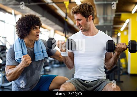Fitness, sport, exercising concept. Fit man exercising together with his personal trainer in gym. Stock Photo