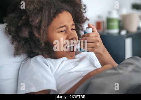 Curly-haired gorl sparying a medicine into her throat Stock Photo