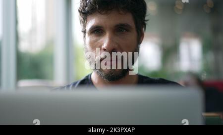 Man staring at laptop screen seated at coffee shop. Person looking at computer with serious expression browsing internet online Stock Photo