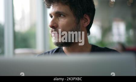 Man staring at laptop screen seated at coffee shop. Person looking at computer with serious expression browsing internet online Stock Photo