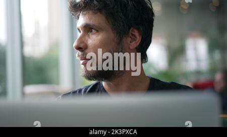 Man staring at laptop screen seated at coffee shop. Person looking at computer with serious expression browsing internet online Stock Photo