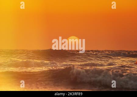 Sun shining over horizon at sunset or sunrise. Evening sea. Ocean water foam splashing. Ocean waves in warm colors sunset sunrise sky lights. Ripple Stock Photo