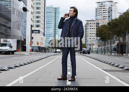 Senior man, businessman talking on the phone while standing on the street with hand on pocket Stock Photo