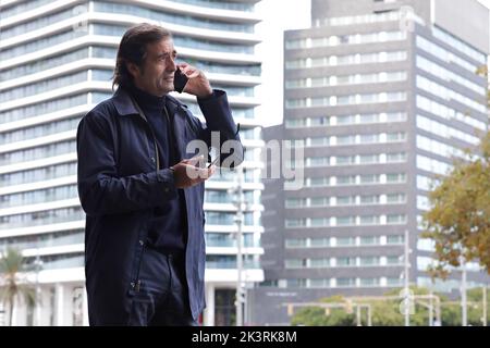 Senior man, businessman talking on the phone while walking around the city holding an eyeglasses Stock Photo