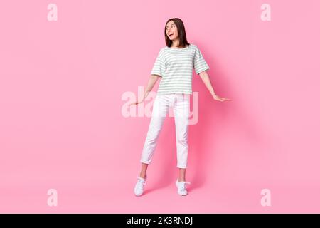 Full size photo of pretty positive girl striped t-shirt white pants shoes interested looking empty space isolated on pink color background Stock Photo