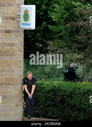 A man was shot just outside Finspång, Sweden. Shortly afterwards, the police managed to arrest a suspect outside the police station in Finspång. The picture shows a police officer, with a weapon, about to arrest the suspect. Stock Photo