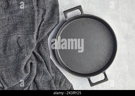 Black cast iron empty frying pan and gray kitchen towel on a gray concrete background Stock Photo