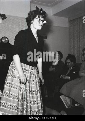 1956, historical, post-war Britain and a lady taking part in a party game, ...knees on the floor hands holding her dress, with a spoon in her mouth balancing a litte ball, England, UK. Stock Photo