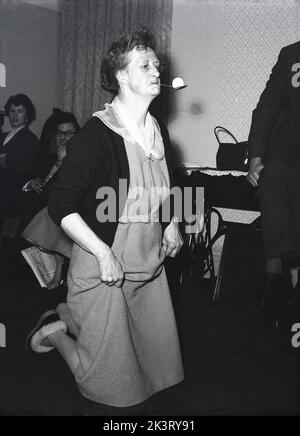 1956, historical, post-war Britain and a lady taking part in a party game, ...knees on the floor hands holding her dress, with a spoon in her mouth balancing a litte ball, England, UK. Stock Photo