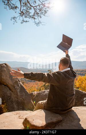 man freelancer working on laptop on the top of the rock with beautiful view of autumn forest Stock Photo