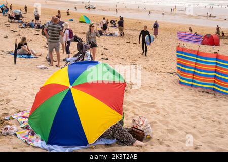 Holidaymakers and colourful umbrellas and windbreaks on a busy Fistral ...