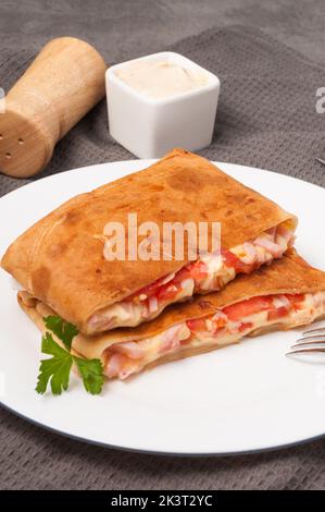 tasty pancakes with ham, cheese and tomatoes on a white plate. vertical frame Stock Photo