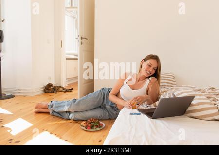 Young woman holding orange juice near laptop and breakfast in bedroom,stock image Stock Photo