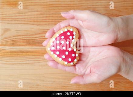 Red and white heart shaped royal icing cookie in woman's hand on wooden background Stock Photo