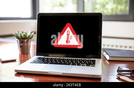 High temperature warning sign on a laptop screen.  Computer overheating concept. Heavy load and hot weather danger. Business office desk background. Stock Photo