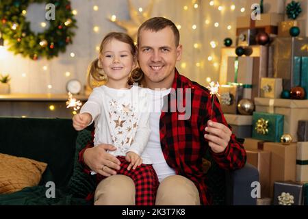 Daughter and father with sparklers in hands sitting on sofa at home Stock Photo