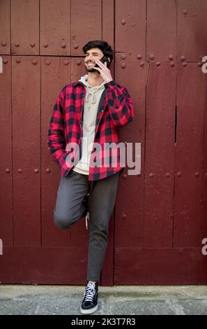 Full body of positive male tourist having phone conversation while standing near red wall of ancient building during trip in town Stock Photo