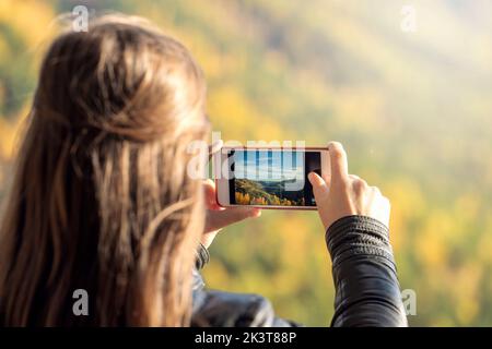 a young woman takes pictures of nature on a smartphone, a view from the back. active lifestyle and impressions. Stock Photo